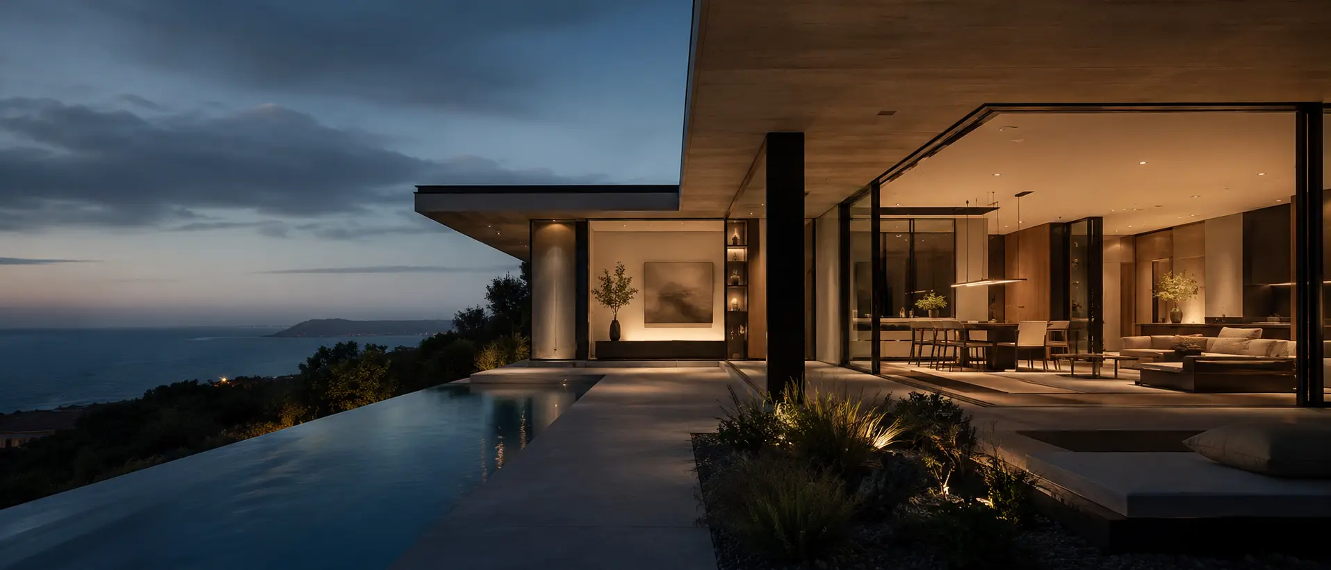 Contemporary residence at dusk, warm interior light opening onto an infinity pool and dark water